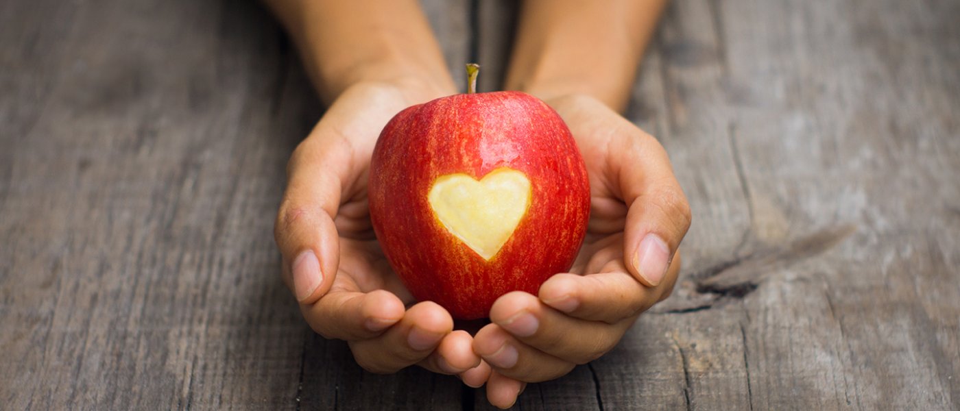 Två händer håller i ett rött äpple som har formen av ett hjärta utskuret från skalet