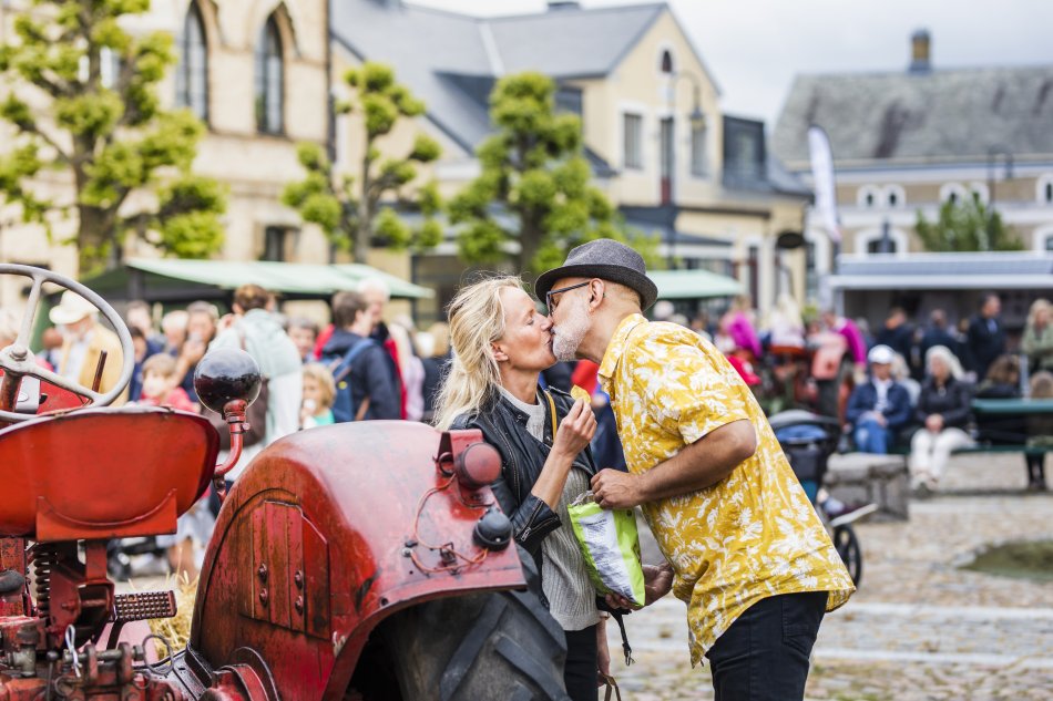 Ett par pussas stående på ett torg och bredvid en traktor. I bakgrunden syns ett myller av besökare på ett evenemang.