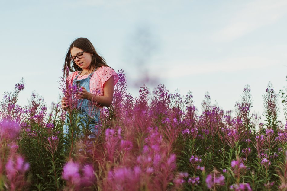 En flicka står i ett blommande fält med rosa blommor. Foto.