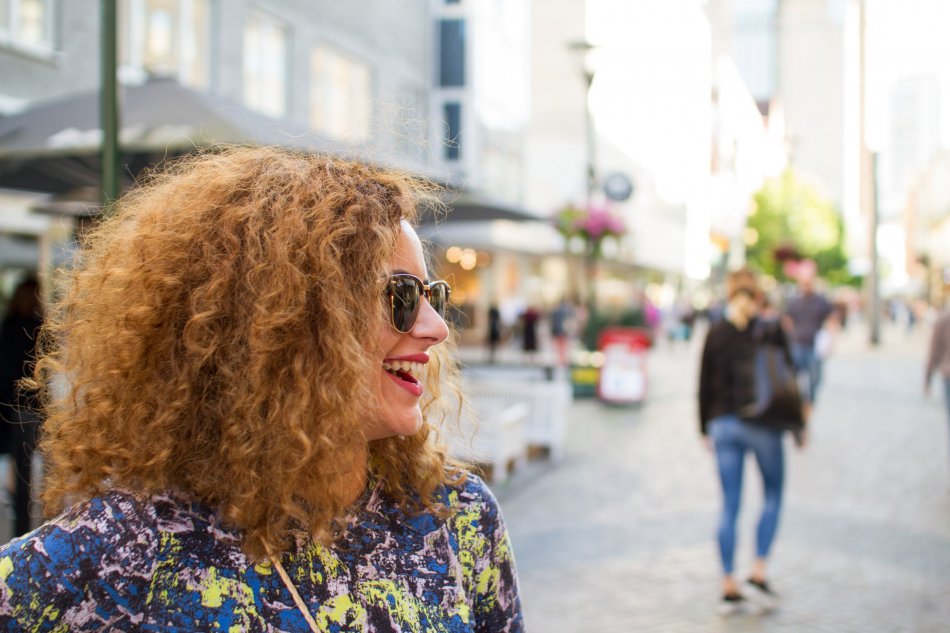 Leende kvinna med krulligt hår och solglasögon på gågata
