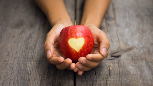 Ett rött äpple med formen av ett hjärta utskuret i skalet vilar i två kupade händer